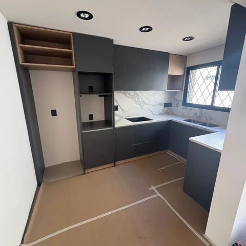 Cocina en U durante la instalación, con frentes grafito, nichos de aspecto madera, mesada clara y piso protegido.